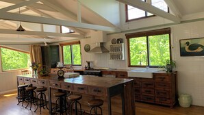 A spacious kitchen with a large island, wooden bar stools, and a view of greenery through the windows. - The Grange Berrima - The Ultimate Rural Retreat. Sleeps up to 13. (Berrima)