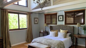 A bedroom with a large bed, wooden headboard, two bedside tables with lamps, a window with curtains, and a chandelier. - The Grange Berrima - The Ultimate Rural Retreat. Sleeps up to 13. (Berrima)