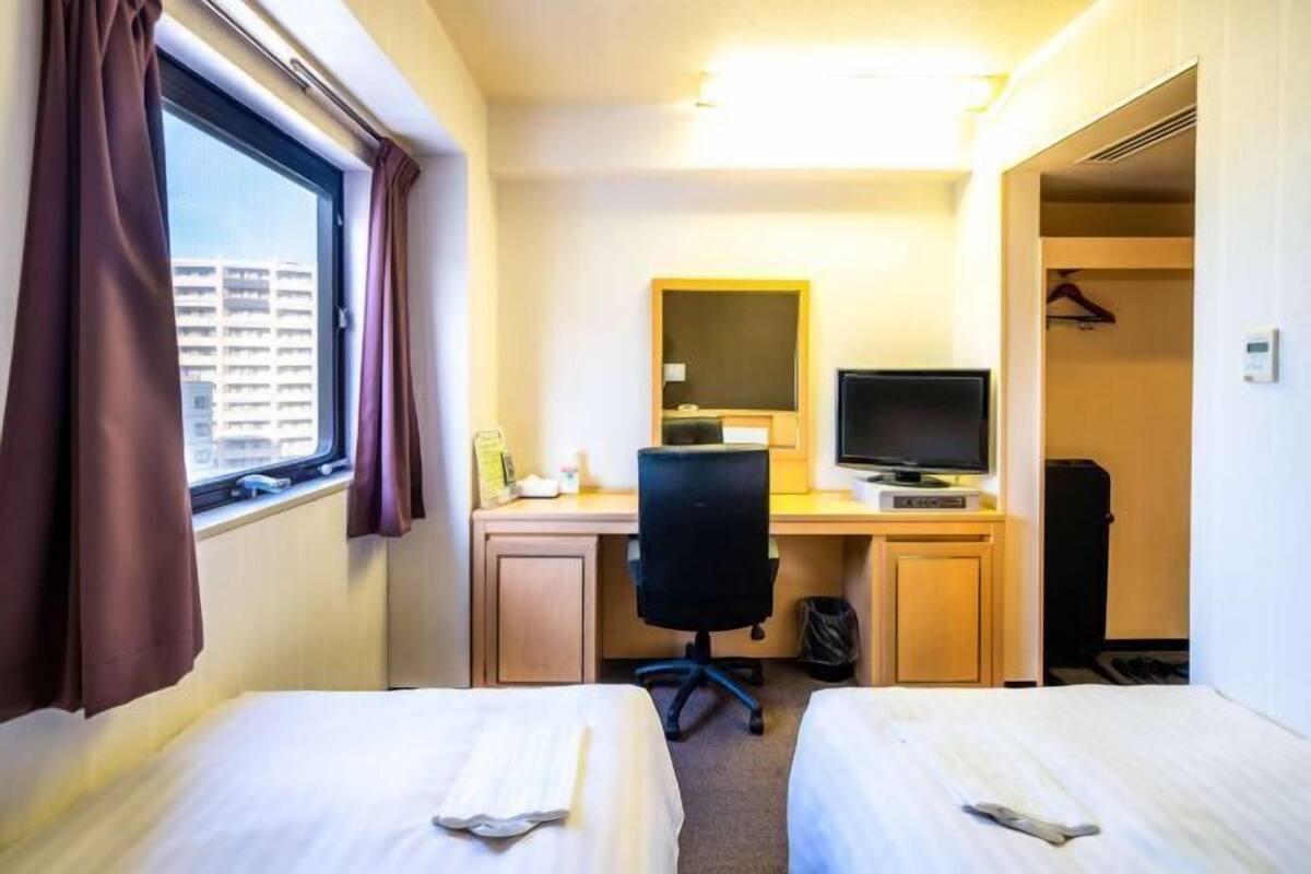 Une chambre d’hôtel avec deux lits, un bureau avec un ordinateur, une télévision et une fenêtre avec des rideaux.