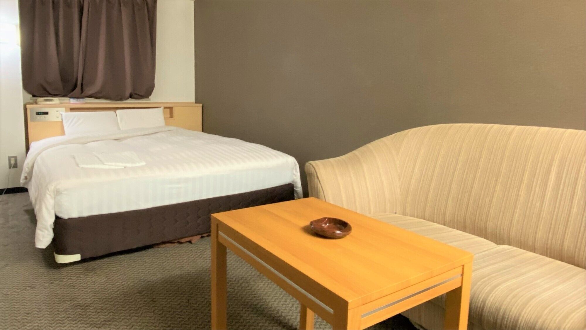 Ein Hotelzimmer mit Bett, Nachttisch mit Schale, Sofa und einem Vorhangfenster.