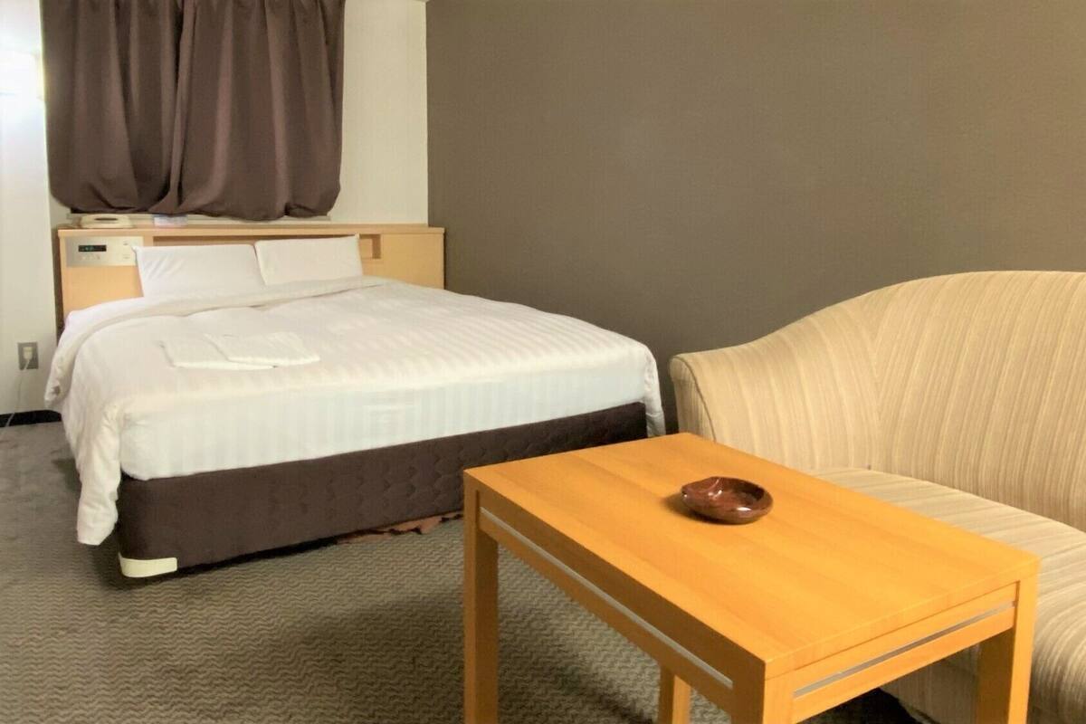 Une chambre d’hôtel avec un lit, une table de chevet sur laquelle se trouve un bol, un canapé et une fenêtre avec des rideaux.