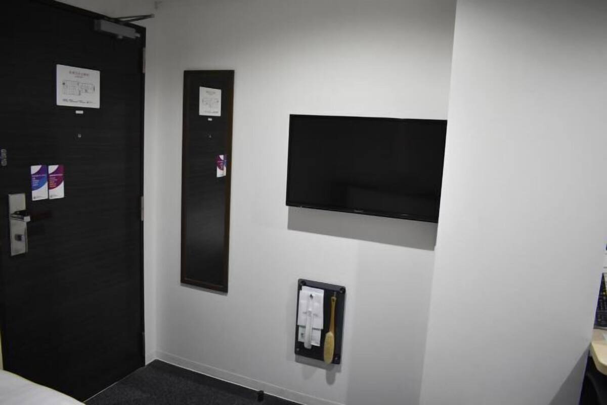 Une chambre d’hôtel avec une porte sombre, un téléviseur fixé au mur et un téléphone mural.