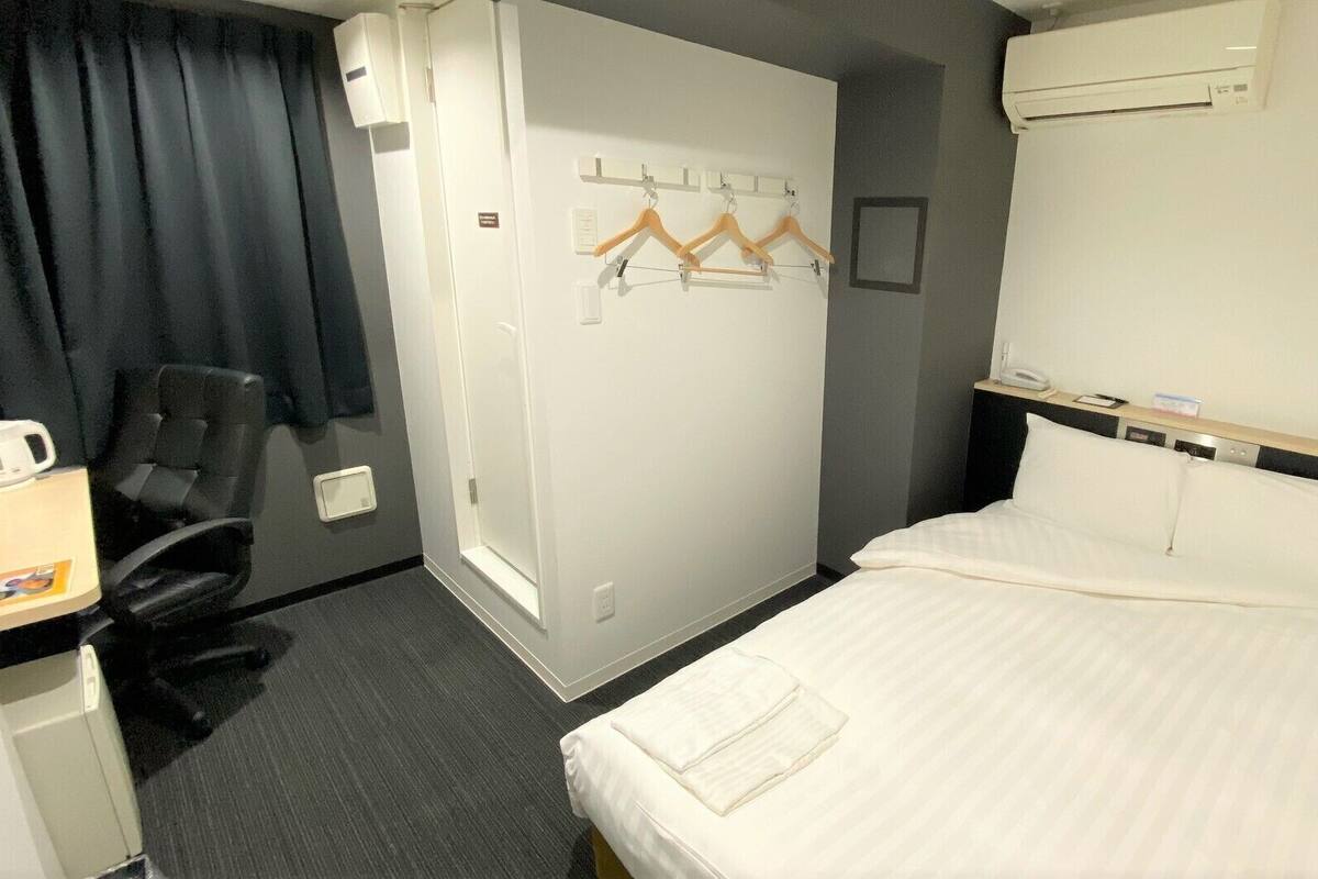 Une chambre d’hôtel comprenant un lit, un bureau avec une chaise, un porte-manteau et un climatiseur fixé au mur.