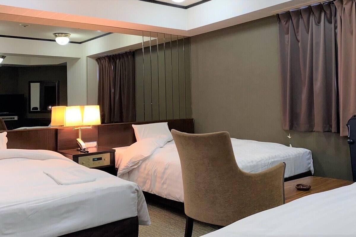 Une chambre d’hôtel avec deux lits, un bureau, une chaise, une lampe et un grand miroir.