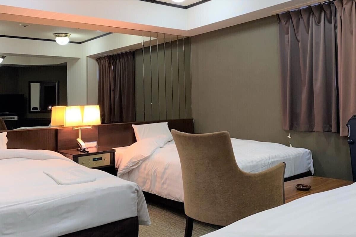 Une chambre d’hôtel avec deux lits, un bureau, une chaise, une lampe et un grand miroir.