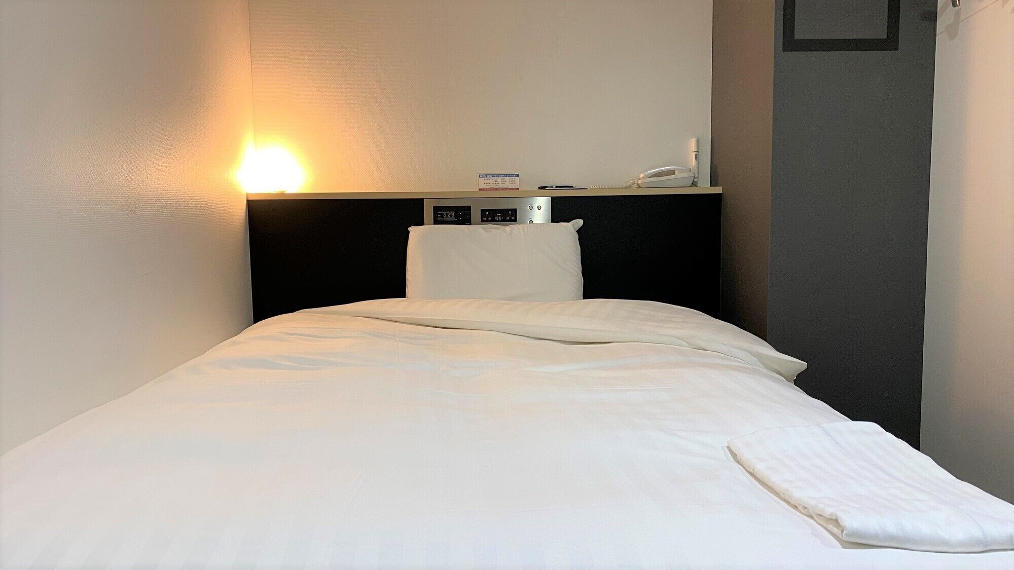 Ein Hotelzimmer mit Bett, Nachttisch mit Telefon und einer fest installierten Bedienkonsole an der Wand.