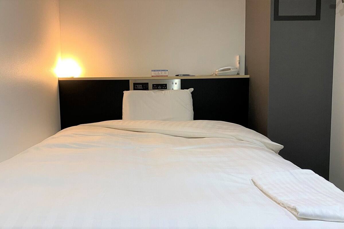 Une chambre d’hôtel équipée d’un lit, d’une table de chevet avec un téléphone et d’un panneau de commande fixé au mur.