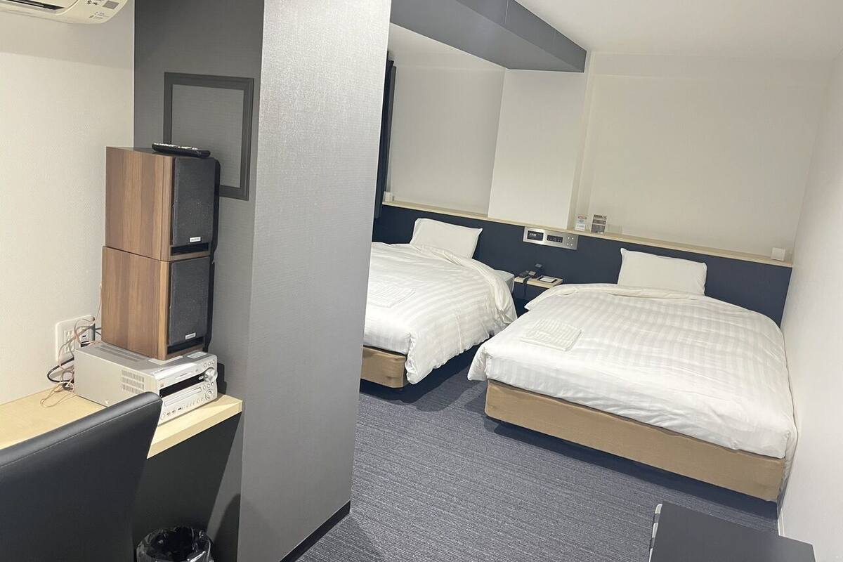 Une chambre d’hôtel avec deux lits, un bureau avec un ordinateur, un miroir et un climatiseur fixé au mur.