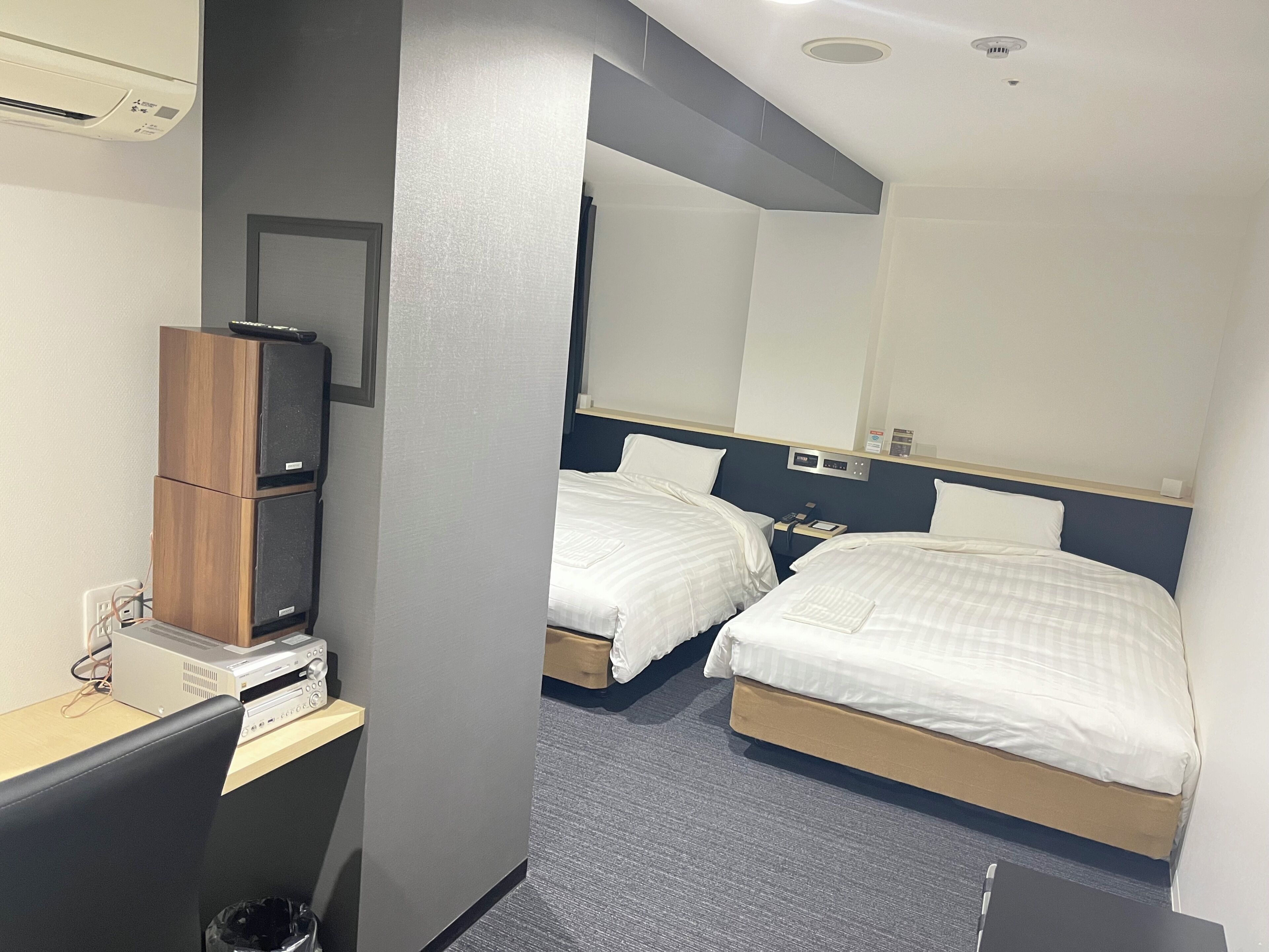 Habitació d'hotel amb dos llits, un escriptori amb un ordinador, aire condicionat i un mirall.