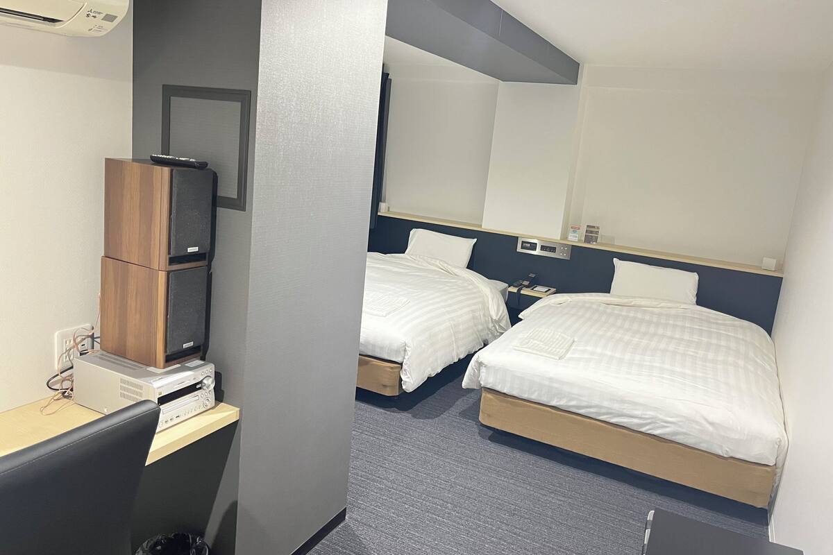 Une chambre d’hôtel avec deux lits, un bureau avec un ordinateur, un climatiseur et un miroir.