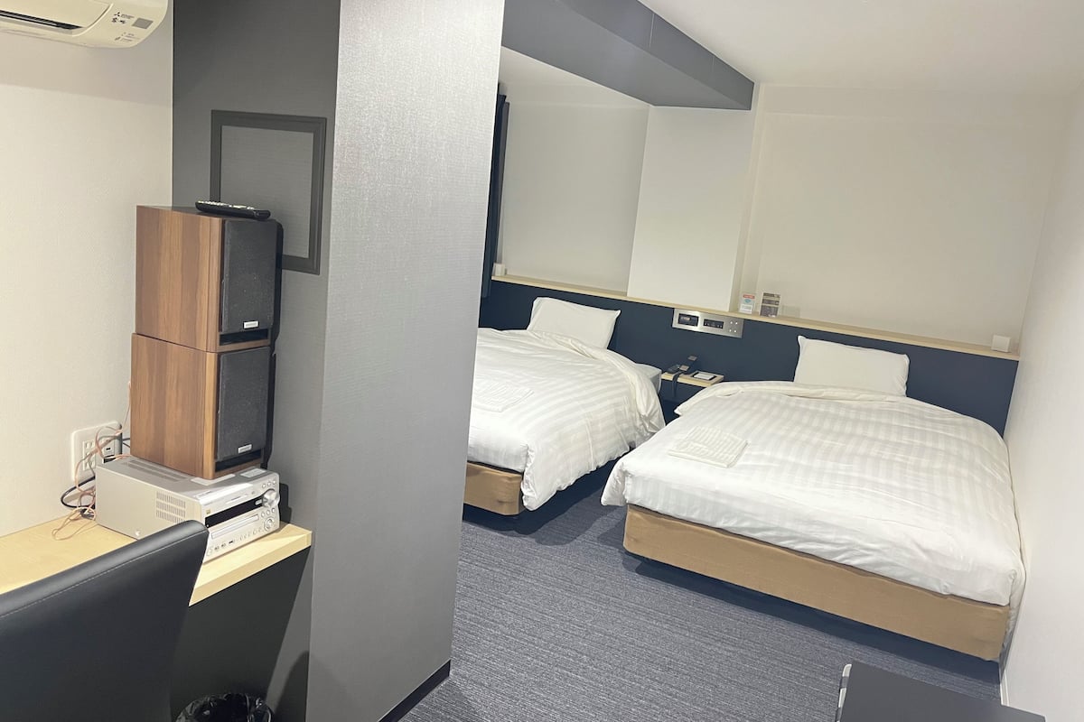 Une chambre d’hôtel avec deux lits, un bureau avec un ordinateur, un climatiseur et un miroir.