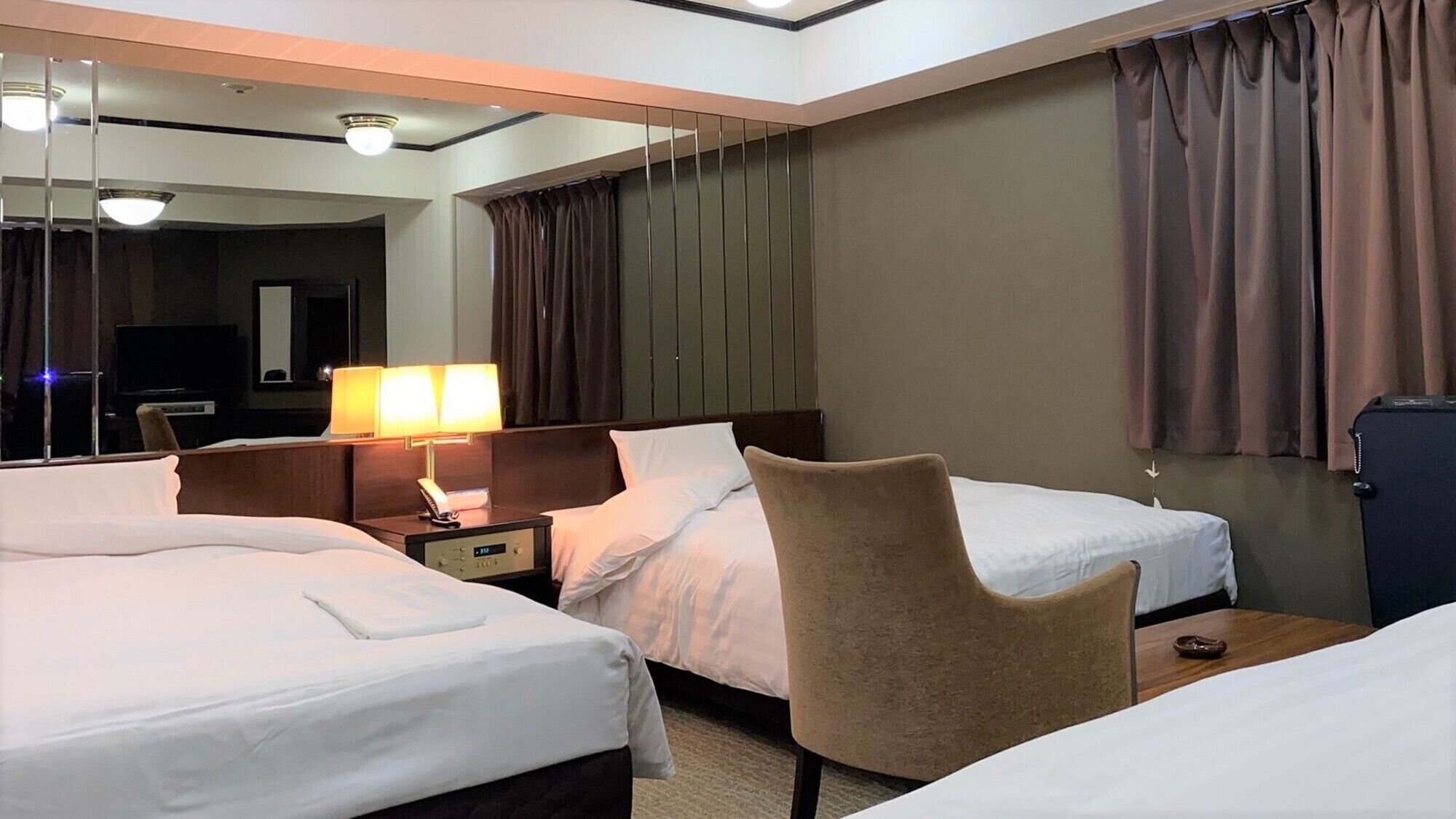 Ein Hotelzimmer mit zwei Betten, einem Schreibtisch, einem Stuhl, einer Lampe, einem Spiegel und einem Fernseher.