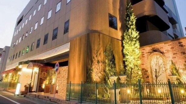 A multi-story hotel with a curved facade, a brick wall, and a large tree in front. - Ramada Encore by Wyndham Amagasaki (Amagasaki)