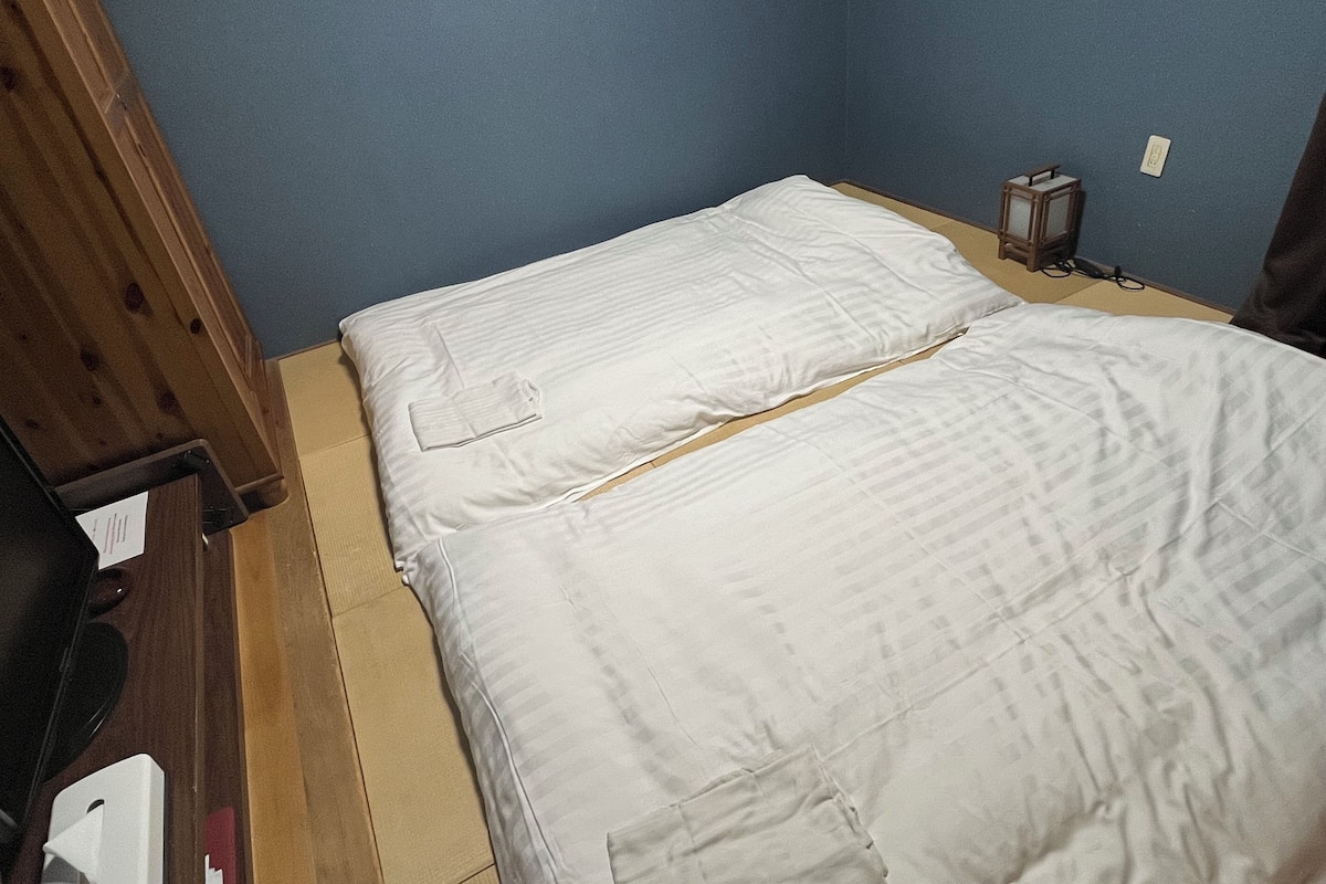 Une petite pièce comprenant un lit, une commode en bois et un luminaire fixé au mur.