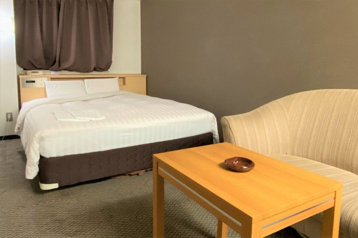Une chambre d’hôtel avec un lit, un canapé, une petite table en bois et une table de chevet avec une lampe.