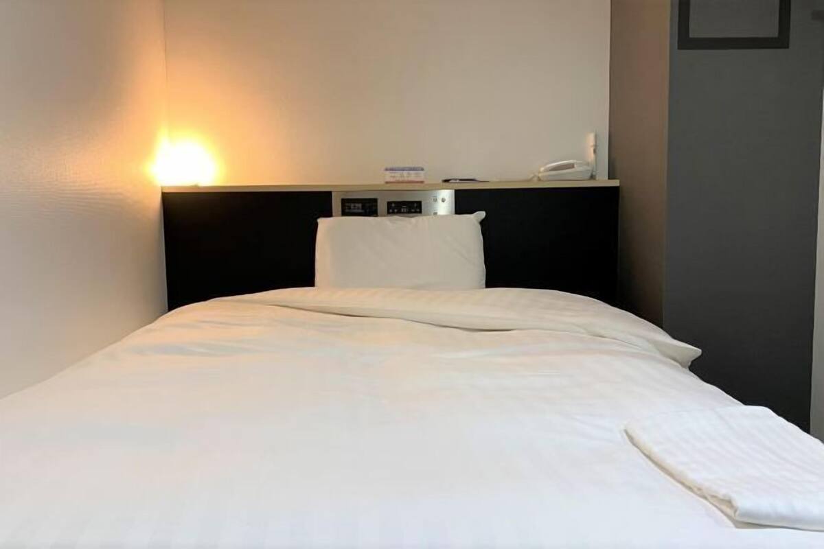 Une chambre d’hôtel comprenant un lit, une table de chevet, une lampe et un thermostat fixé au mur.