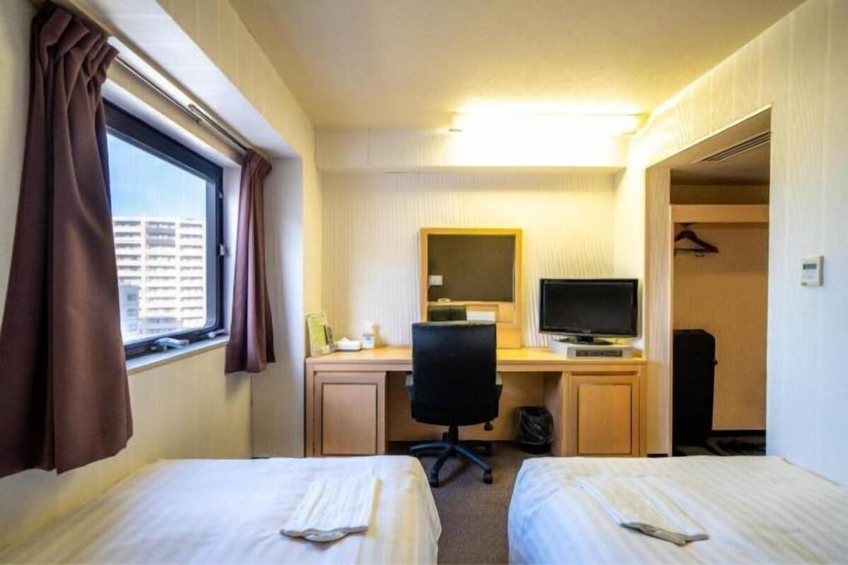 Une chambre d’hôtel avec deux lits, un bureau avec un ordinateur, une télévision et une fenêtre avec des rideaux.