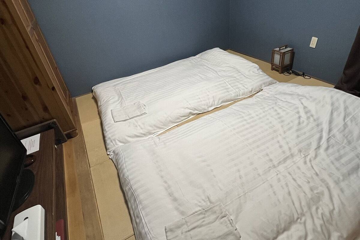 Une petite chambre avec un lit simple, une armoire en bois, une petite table et un luminaire fixé au mur.