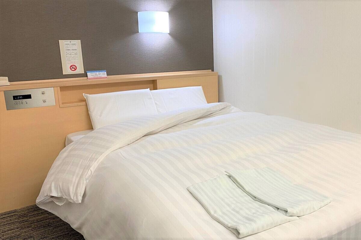Une chambre d’hôtel comprenant un lit, un panneau de commande près du lit, une lampe fixée au mur et un panneau avec du texte.