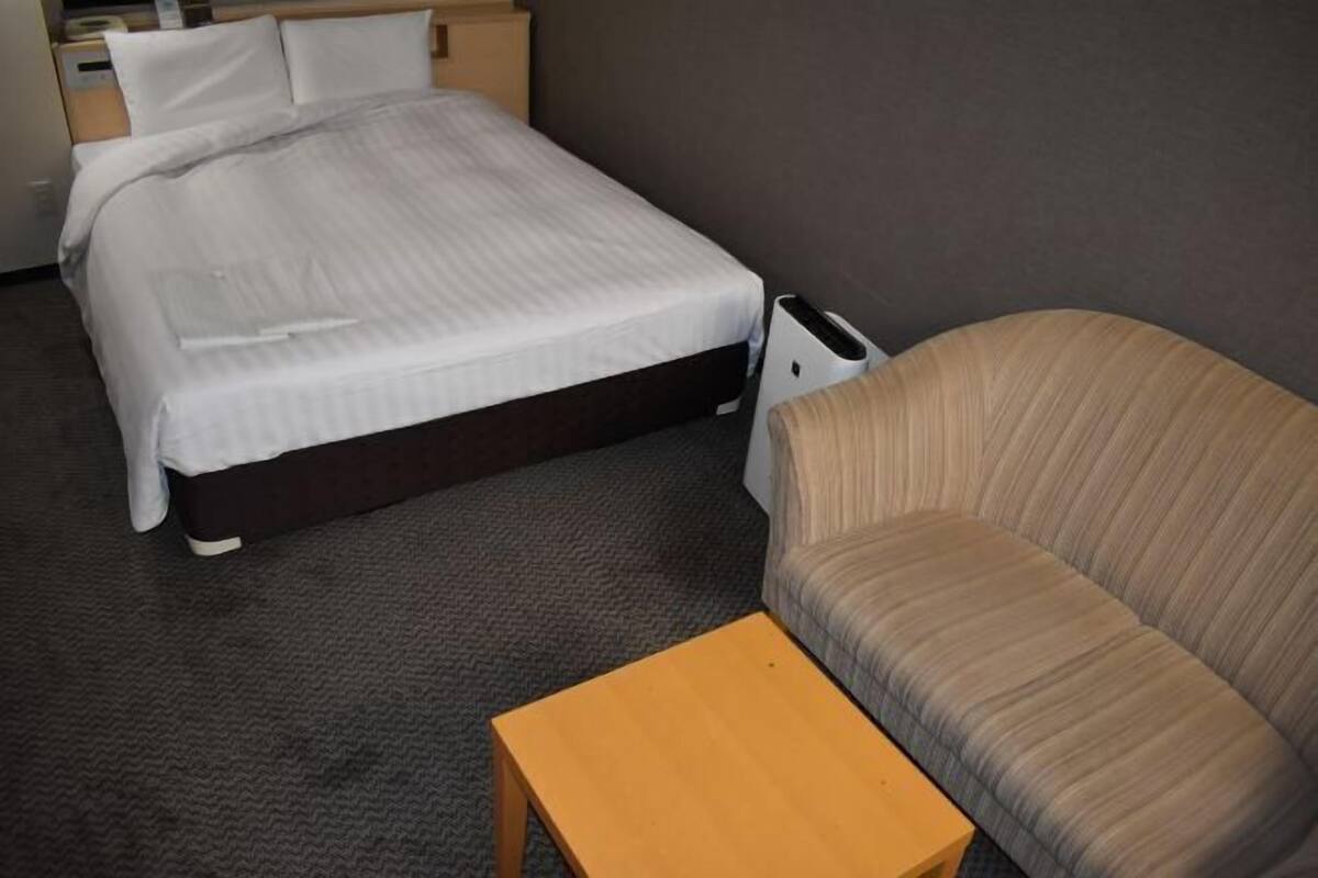 Une chambre d’hôtel avec un lit, une table de chevet, un canapé et un radiateur.