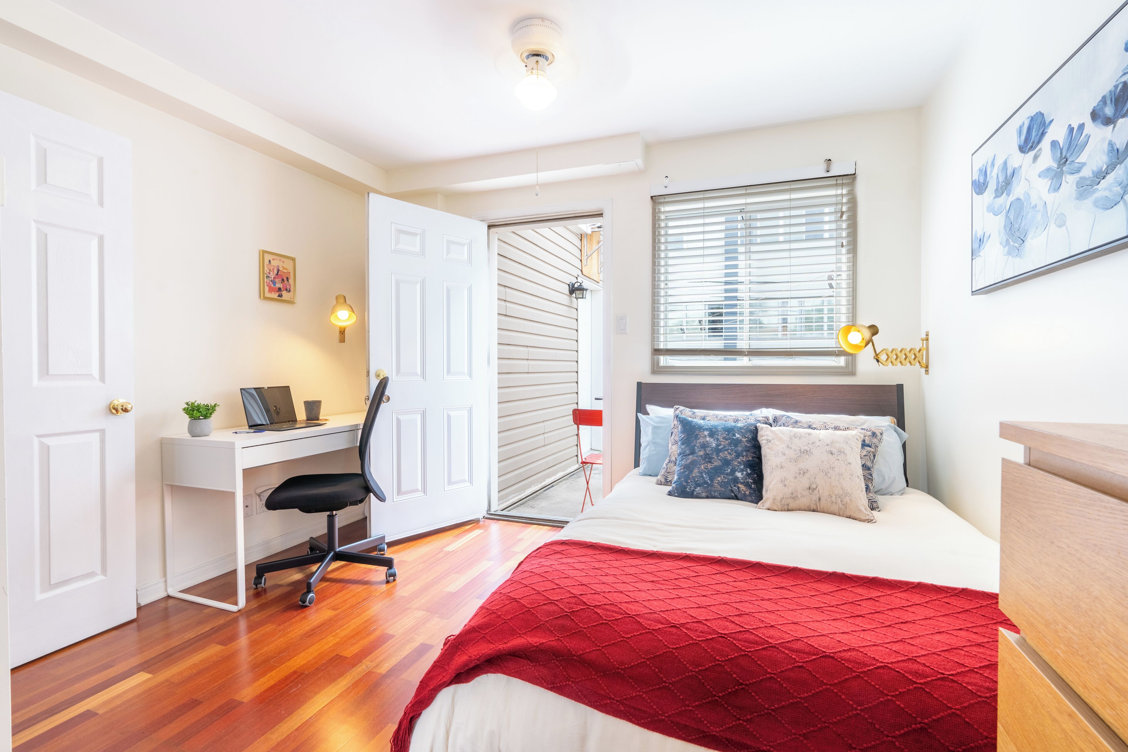 A bedroom with a bed, a desk, a chair, and a window with blinds.