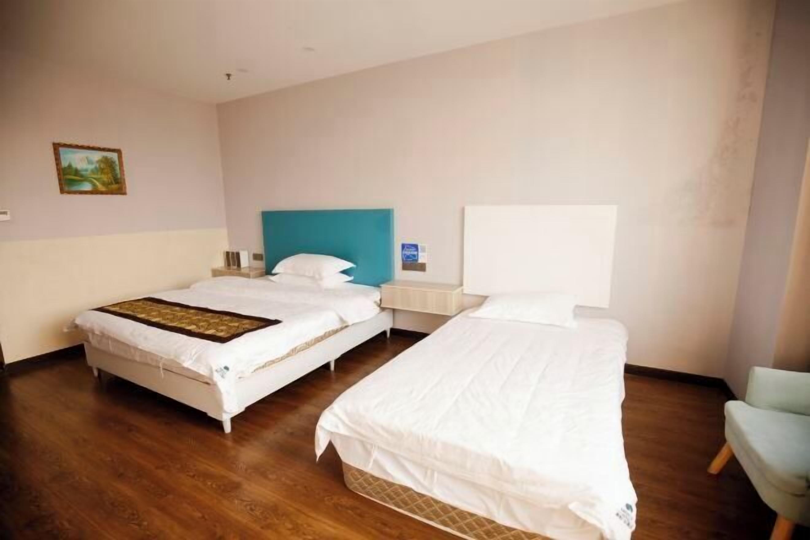 A hotel room with two beds, wooden flooring, a painting on the wall, and a white headboard.