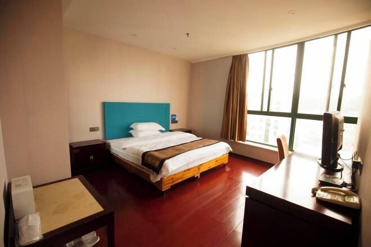 Une chambre d’hôtel avec un lit, un bureau, une chaise, une télévision et une fenêtre avec des rideaux.