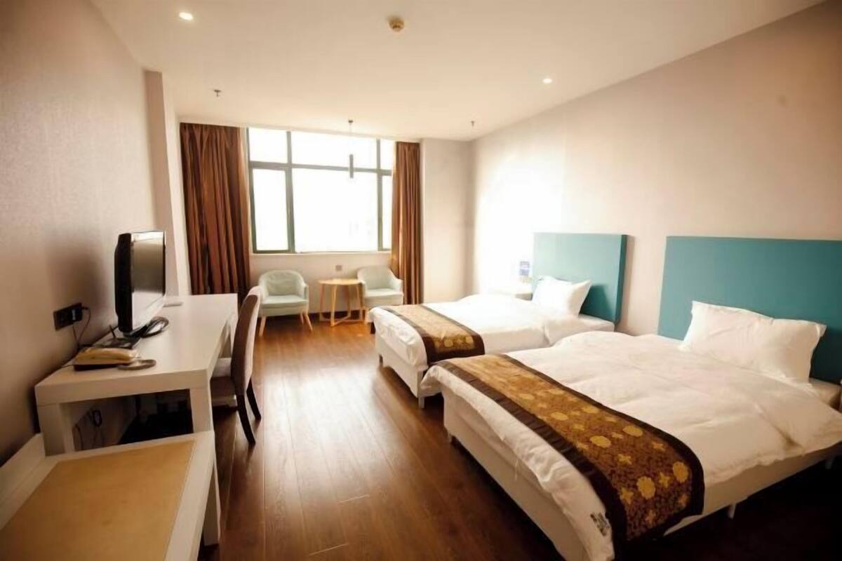 Une chambre d’hôtel avec deux lits, un bureau avec une chaise, une petite table et un téléviseur.