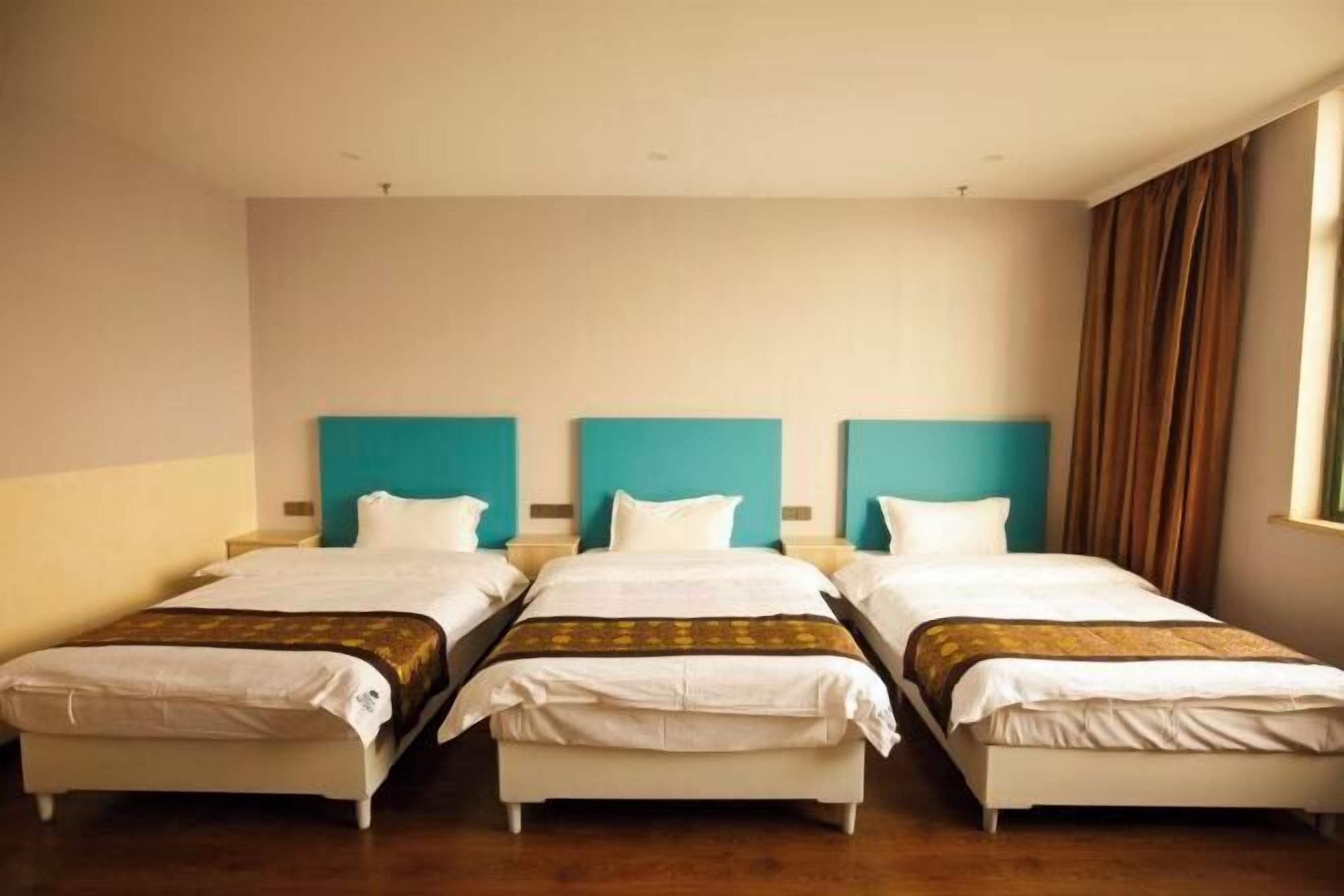 A hotel room with three single beds, a wooden floor, and a window with curtains.