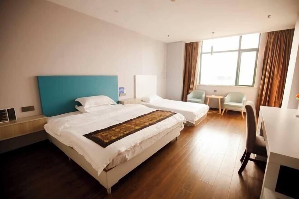 Une chambre d’hôtel avec deux lits, un bureau, une chaise et une fenêtre avec des rideaux.