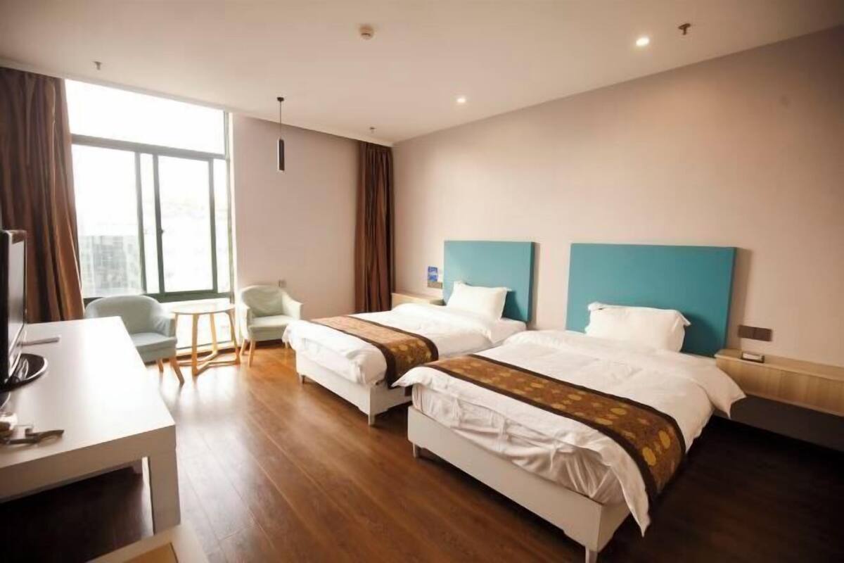 Une chambre d’hôtel avec deux lits, un bureau, une chaise et une grande fenêtre.
