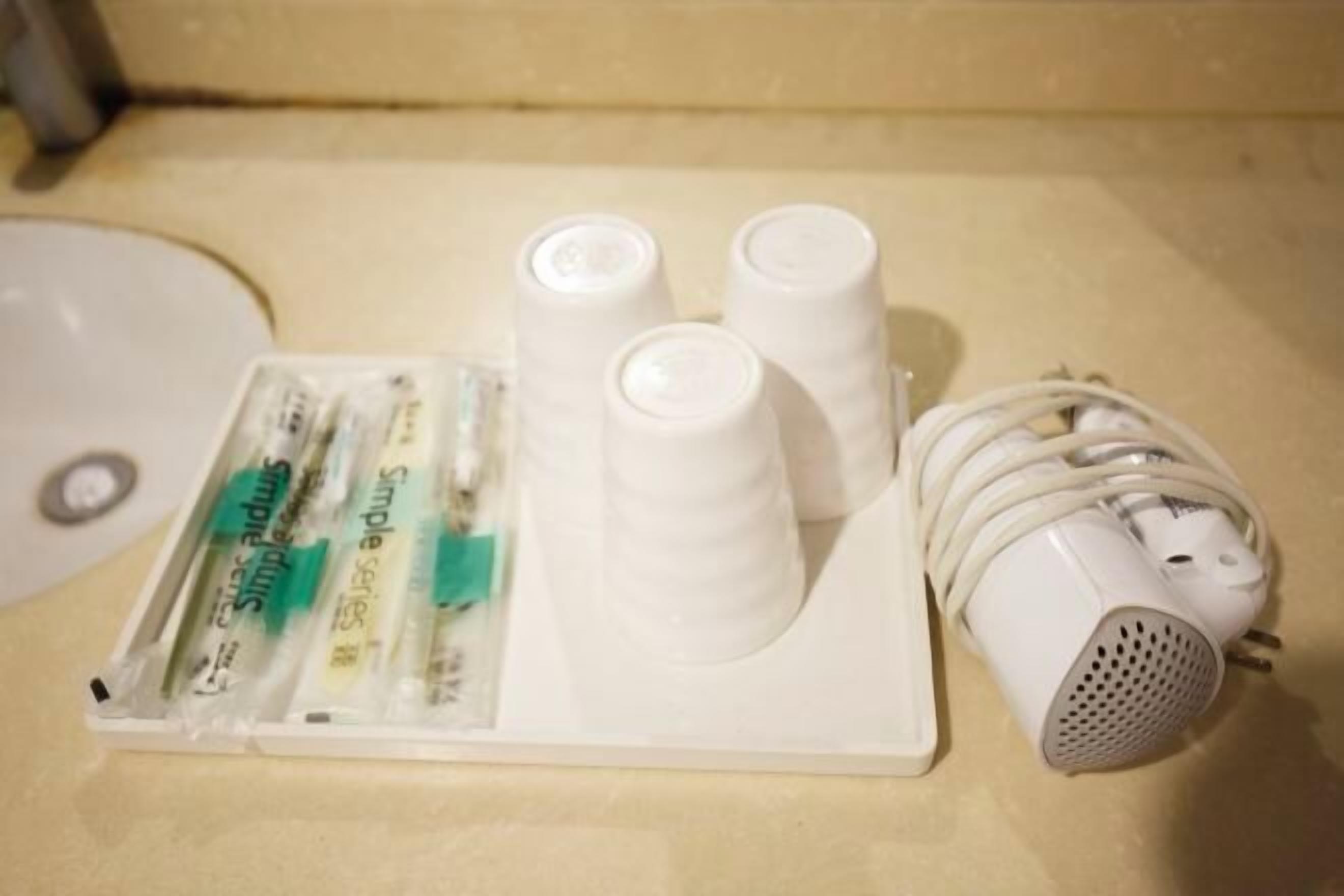 A bathroom with a white sink, a set of white cups, a white speaker, and a package of Simple Series mouthwash.