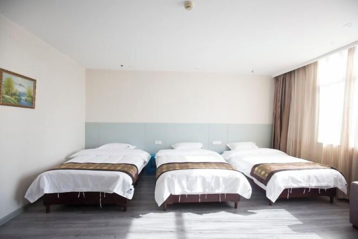 A hotel room with three single beds, a large window with curtains, and a painting on the wall.