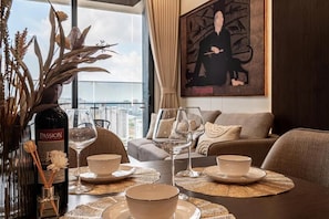 A dining area with a table set for two, a bottle of wine, and a vase with dried flowers.