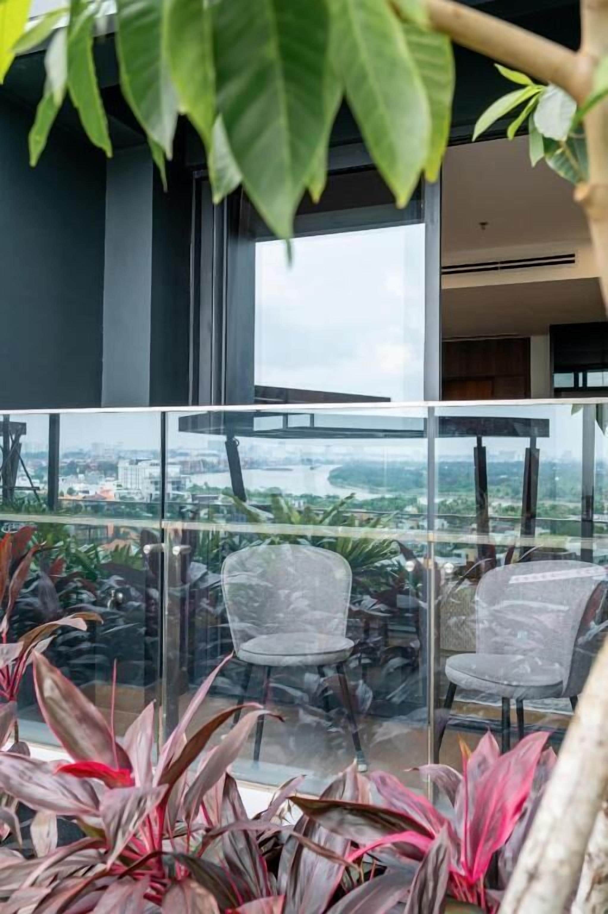 A balcony with glass railings, two chairs, and potted plants.