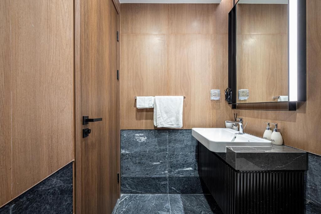 Un baño moderno con tocador de madera, un espejo grande y suelo de baldosas de mármol.