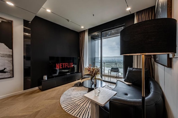 A modern hotel room with a large window, a flat-screen TV, a round coffee table, and a sofa.