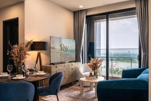 A modern living room with a dining area, a television, and a view of a cityscape through large windows. - Lumiere riverside - Apartment Raymond Holm (Ho Chi Minh City)