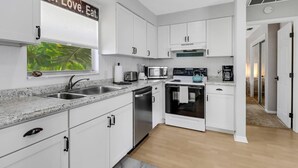 A modern kitchen with white cabinets, stainless steel appliances, and a granite countertop. - Old Florida Waterfront Duplex! Close to Beach! Bikes, Kayak & Over $100 of Free Daily Activities! (Bonita Springs)
