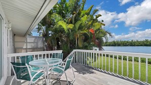 A balcony with a table and chairs, overlooking a lake and surrounded by lush greenery. - Old Florida Waterfront Duplex! Close to Beach! Bikes, Kayak & Over $100 of Free Daily Activities! (Bonita Springs)
