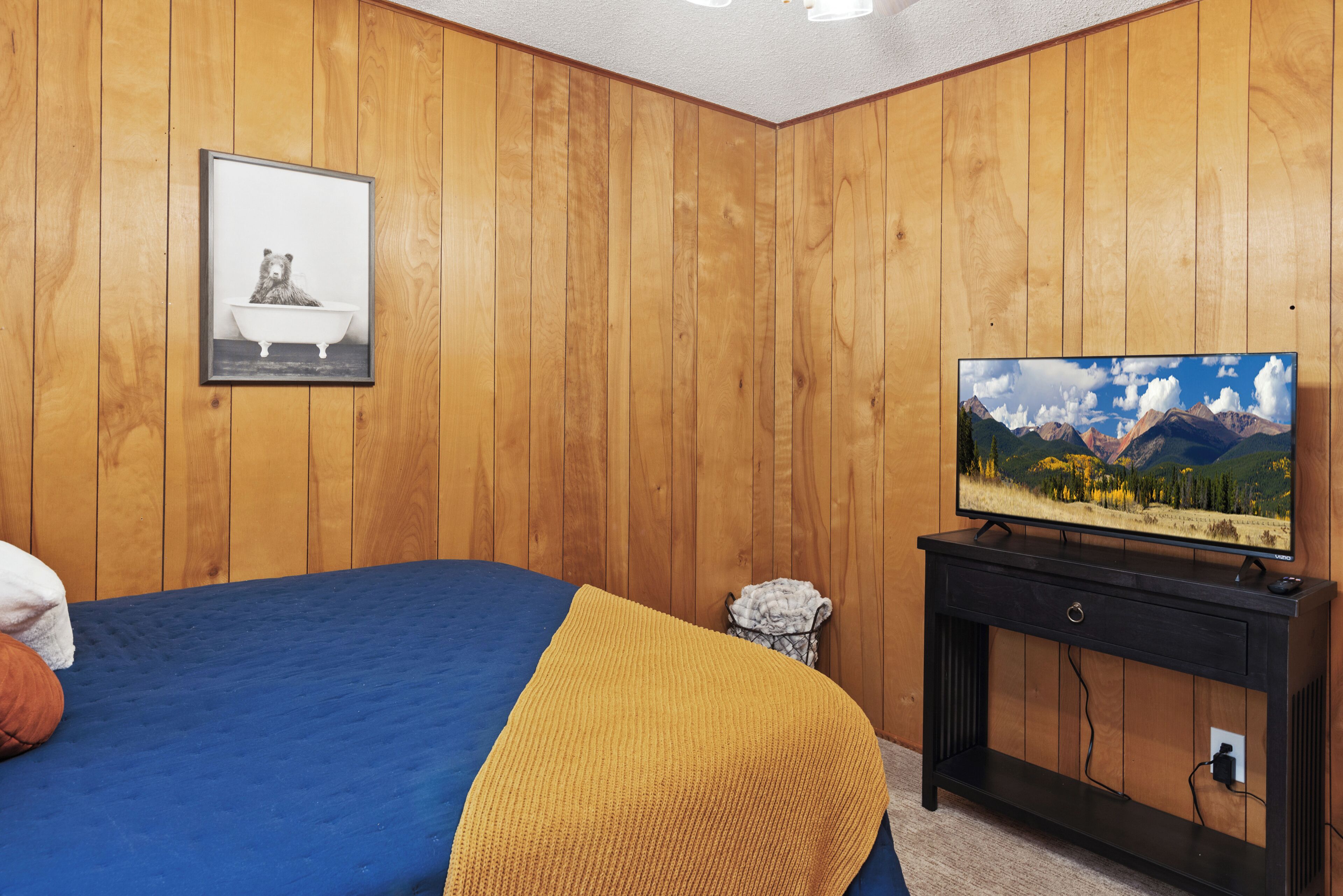Un dormitorio con una cama, un televisor sobre un mueble bajo y paneles de madera en las paredes.