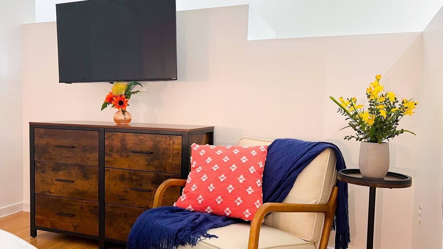 Un salon avec un meuble en bois, un canapé agrémenté d’un coussin à motifs rouges, un plaid bleu et une petite table sur laquelle est posée une plante en pot.