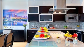 A modern kitchen with a cityscape mural, a glass dining table set with yellow napkins and plates, and a built-in microwave. - Downtown Cleveland: Steps To Sports & Events 2 Bedroom Condo by RedAwning (Cleveland)