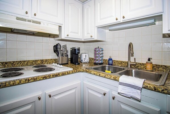 Fully equipped kitchen with double electric stove, stainless steel sink, and coffee maker.