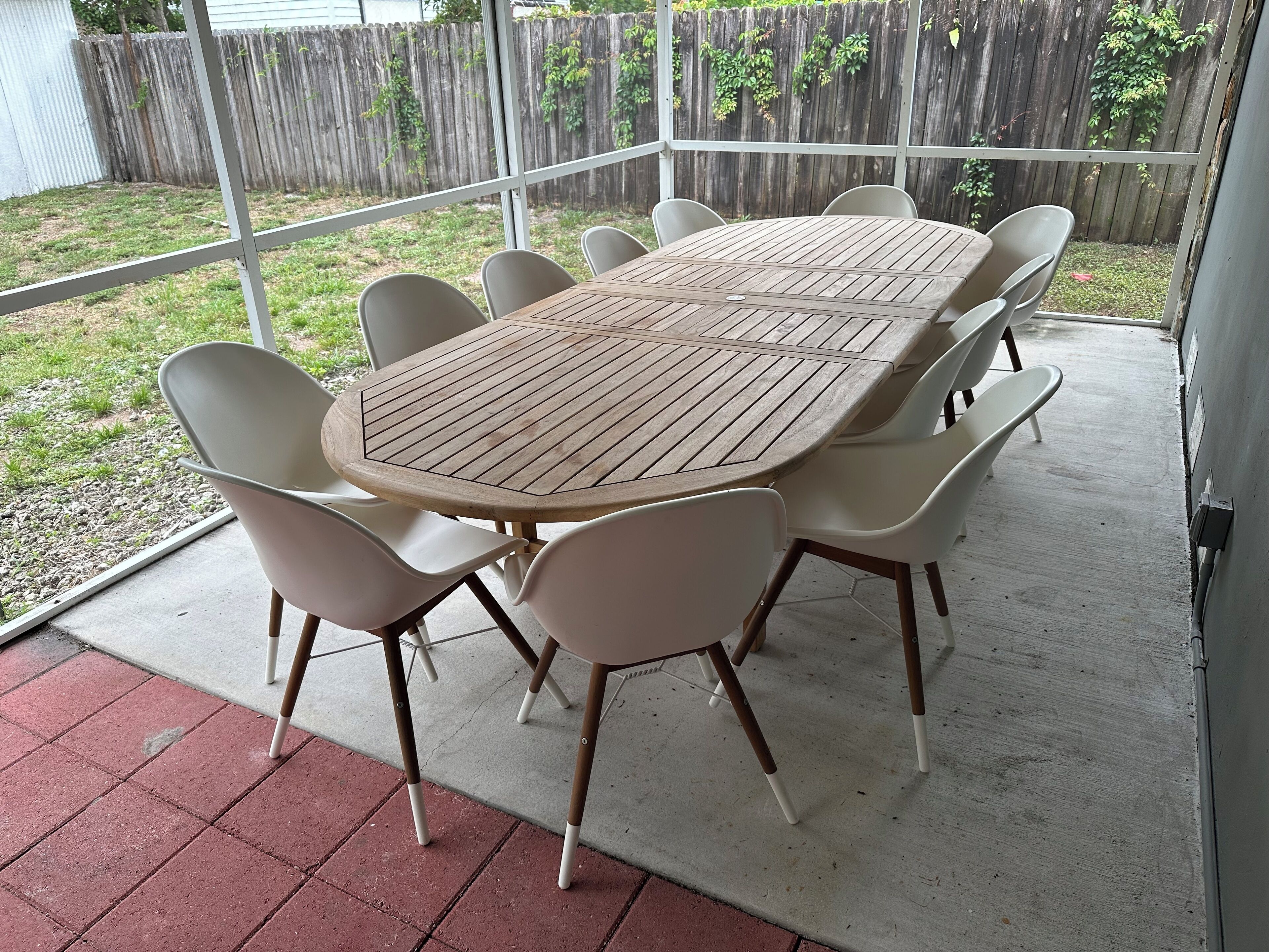Een overdekt terras met een ronde houten tafel en zes witte stoelen.