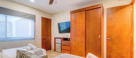 Une chambre d’hôtel avec deux lits, une télévision, un ventilateur de plafond, des armoires en bois et une fenêtre.
