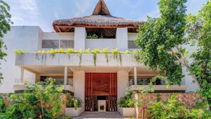 A modern building with a thatched roof, a balcony with plants, and a stone wall. - Aldea Zama Condo: Rooftop Infinity Pool and Spa (Tulum)