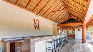 A bar area with a thatched roof, a counter, and bar stools. - Aldea Zama Condo: Rooftop Infinity Pool and Spa (Tulum)