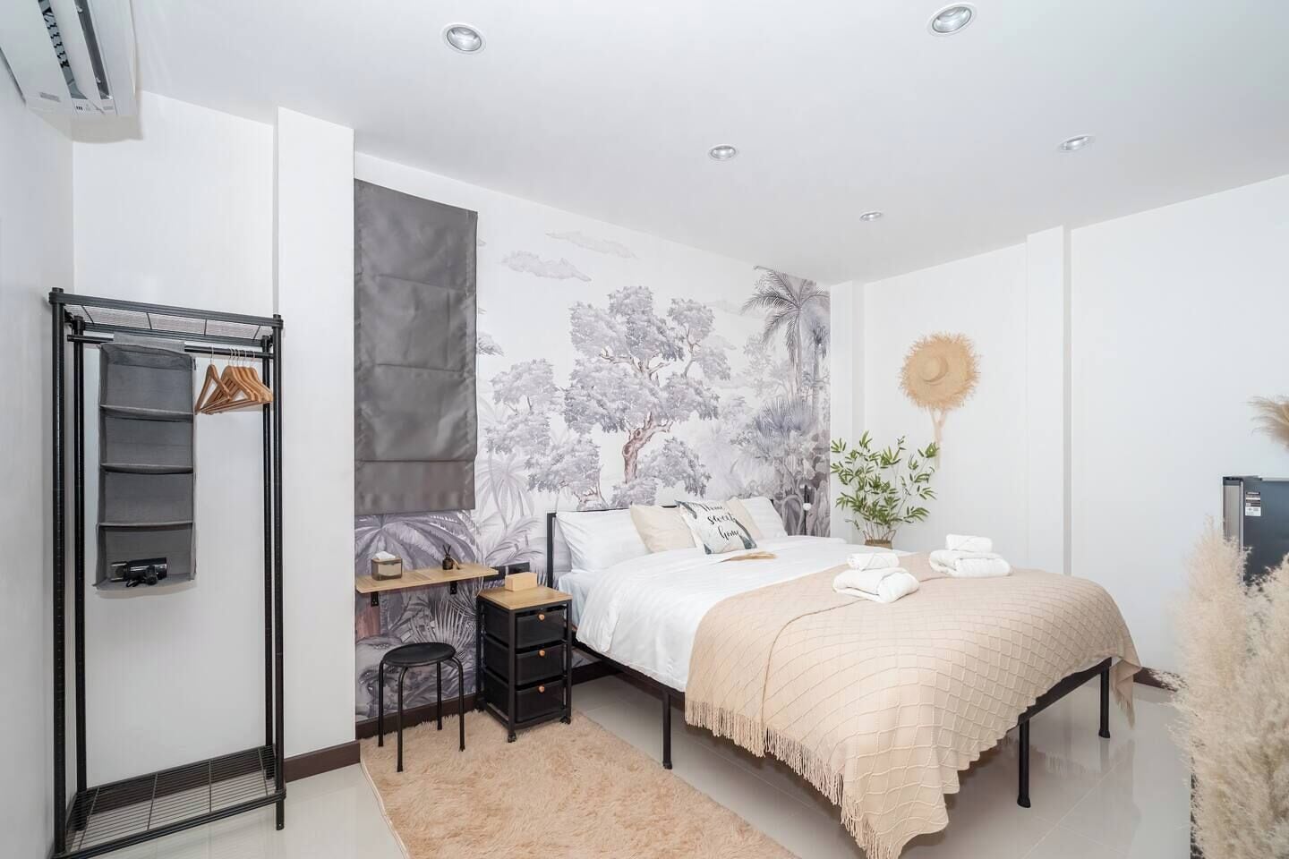 A bedroom with a bed, a nightstand, a shelf unit, and a hanging rack.
