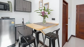 A compact kitchen with a microwave, cabinets, and a sink. There is a wooden table with two chairs and a vase with flowers.